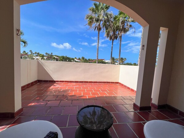 Une terrasse aux carreaux rouges, un tambour et une vue sur des palmiers et des maisons.