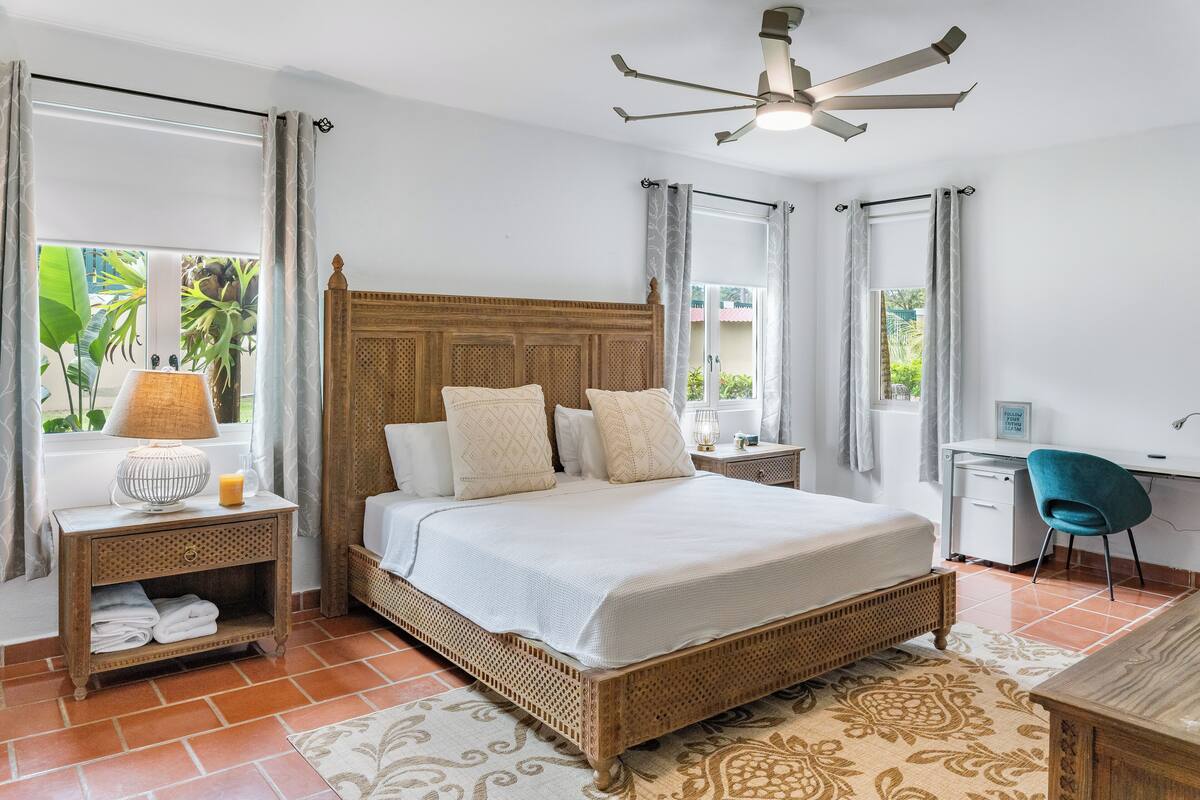 A bedroom with a wooden bed, a desk, a chair, and a window with curtains.