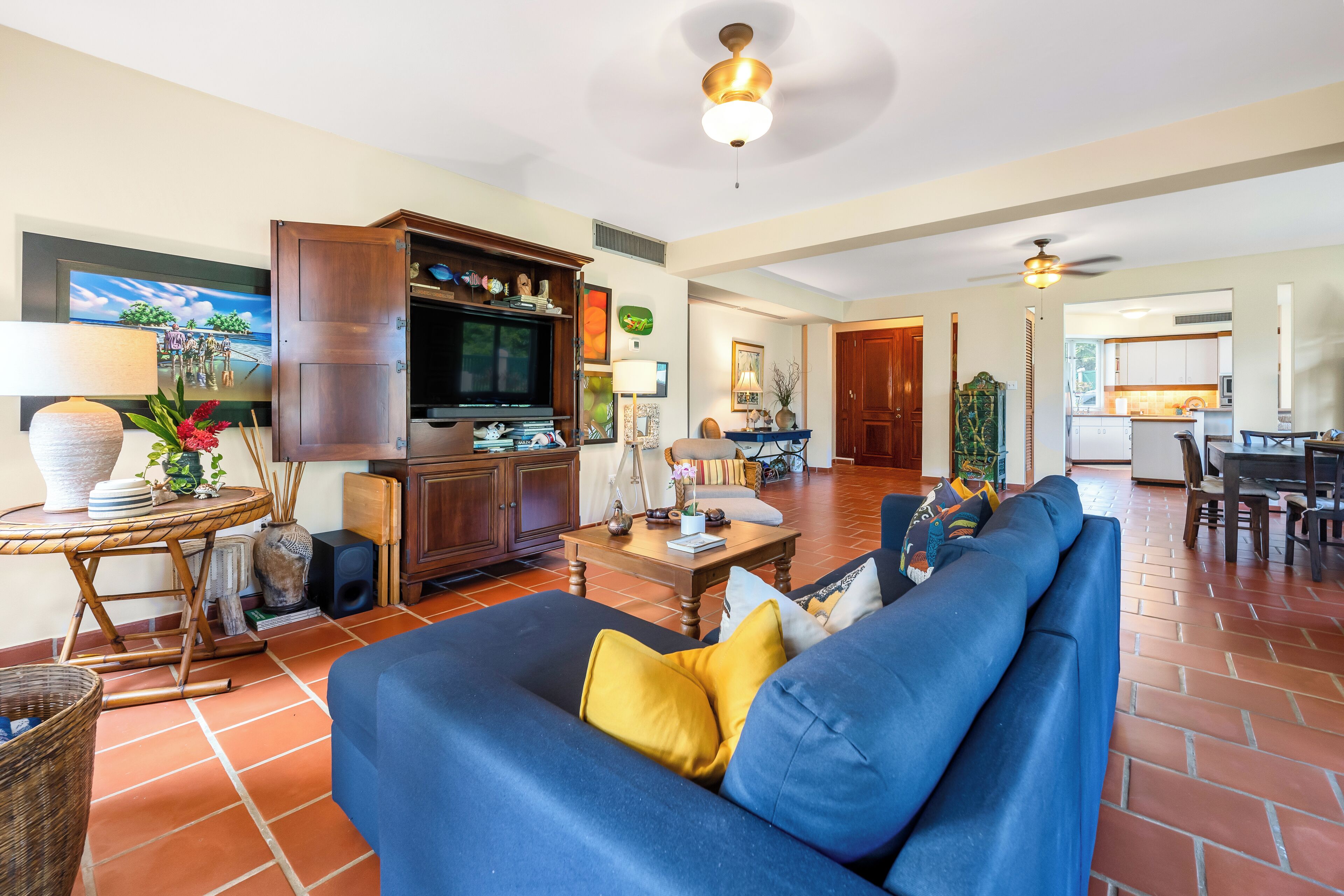 Un salon spacieux avec un canapé bleu, un meuble de rangement en bois et un coin repas à l’arrière-plan.