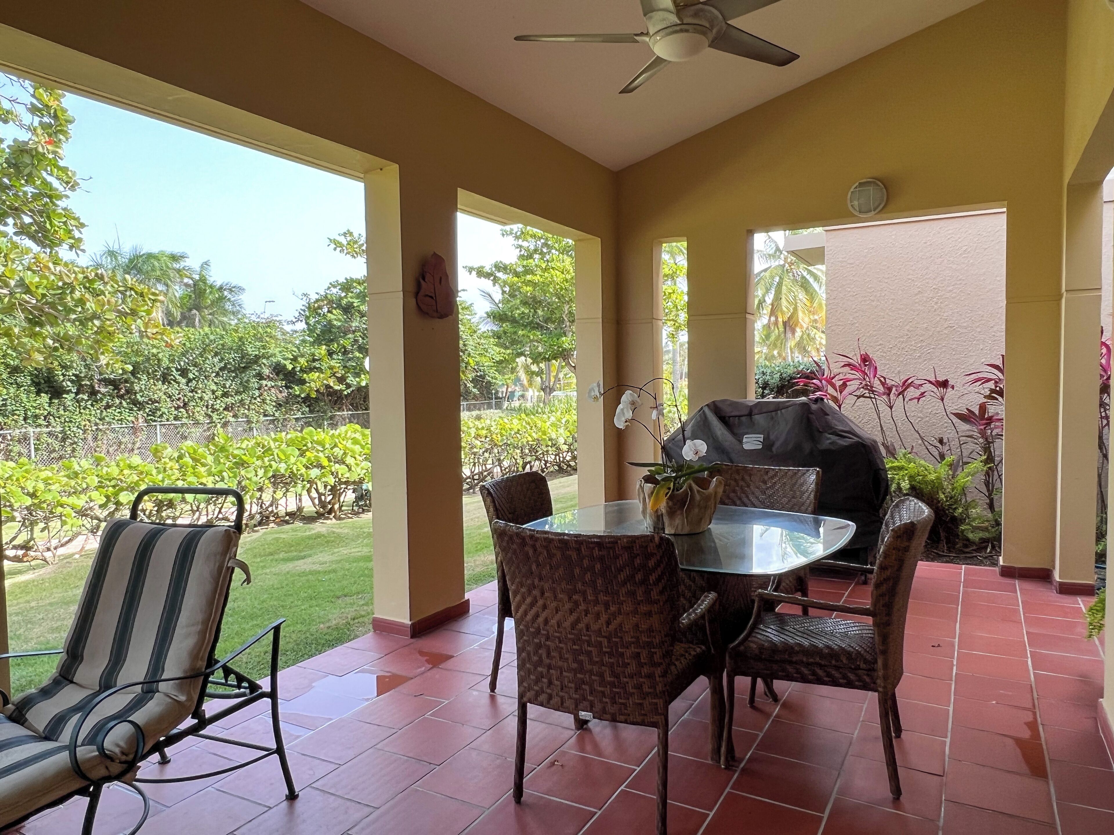 A covered patio with a table and chairs, a ceiling fan, and a view of a garden.