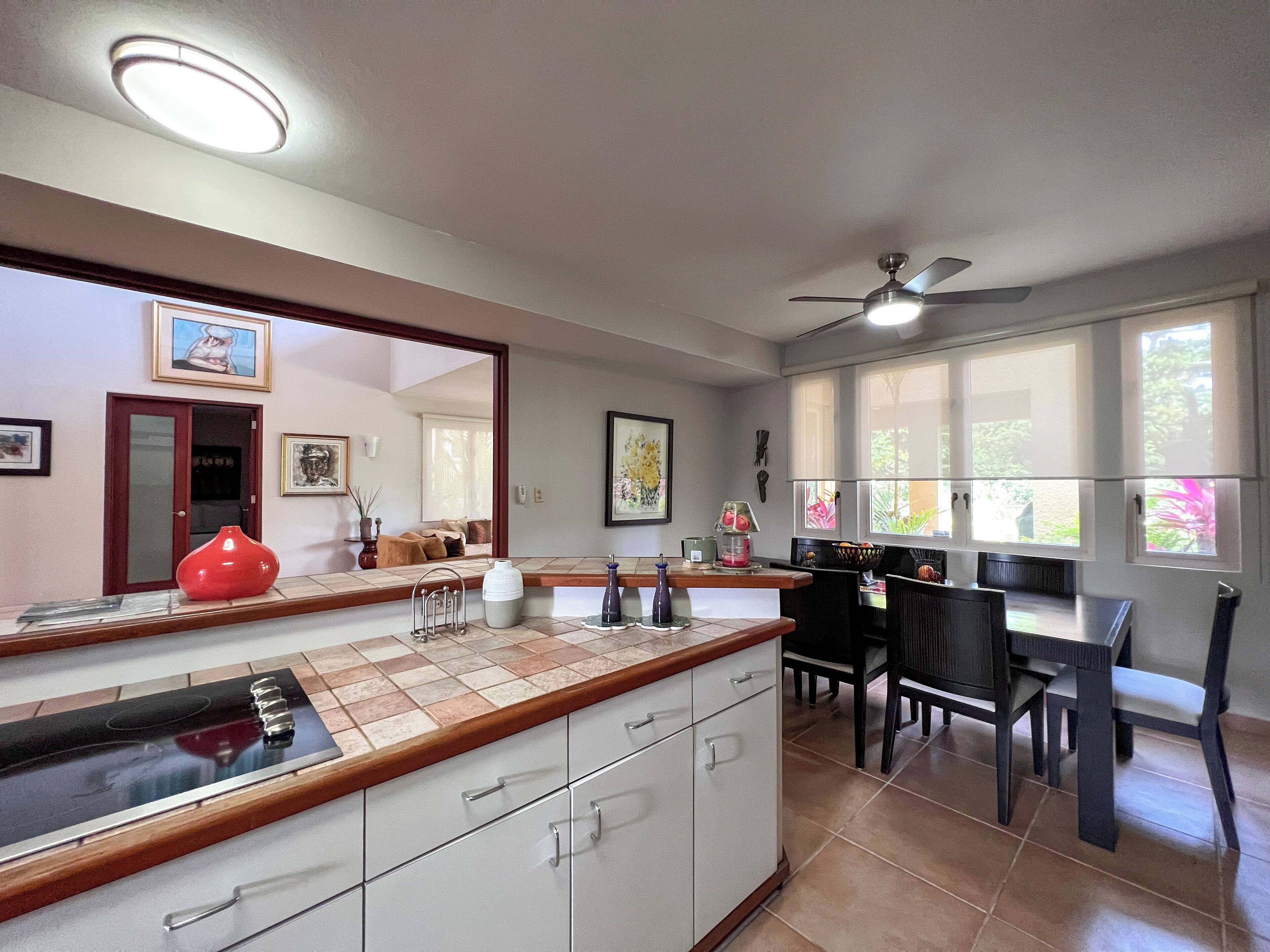 A modern kitchen with a central island, dining area with chairs, and large windows.