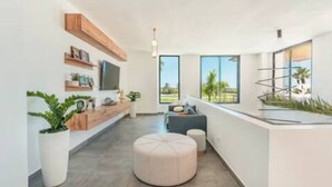 A modern interior with a long hallway, a seating area with a cushioned ottoman, and a large window offering a view of greenery. - Luxury Retreat Condo 3BR Cap Cana Punta Cana (Punta Cana)