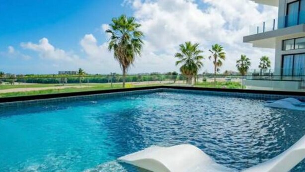 A swimming pool with clear blue water, surrounded by palm trees and a modern building with large windows. - Luxury Retreat Condo 3BR Cap Cana Punta Cana (Punta Cana)