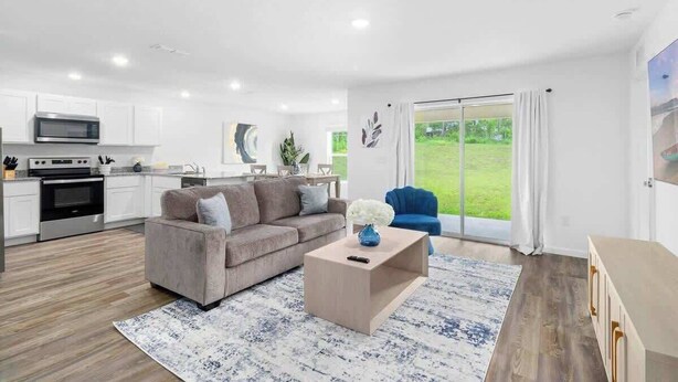 A modern living room with a grey sofa, a coffee table, and a view of a green garden through a sliding glass door. - Spacious House with Garden | Ideal for Long Stays (Spring Hill)
