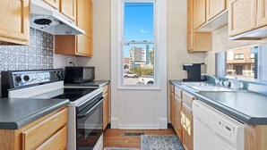 Une cuisine compacte avec des meubles en bois, une cuisinière, un four à micro-ondes et un lave-vaisselle. Une fenêtre offre une vue sur l’extérieur.