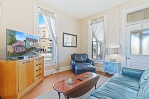 A living room with a wooden cabinet, a blue leather chair, a blue sofa, and a television displaying a house model.