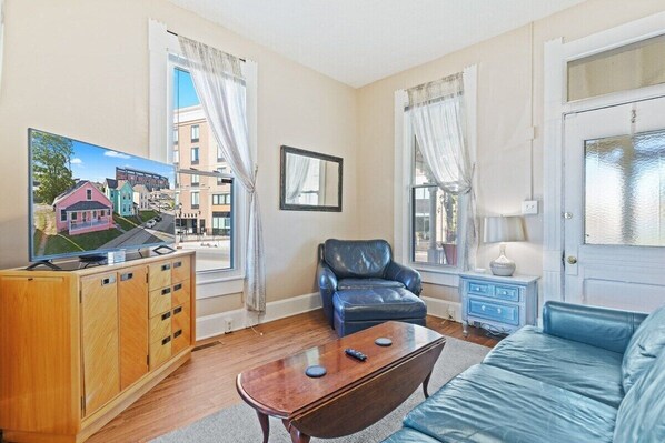 A living room with a wooden cabinet, a blue leather chair, a blue sofa, and a television displaying a house model.