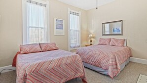 Une chambre à coucher avec deux lits, chacun agrémenté de draps à motifs, d’un ventilateur de plafond et d’un tableau encadré au mur.