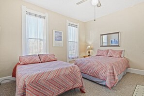 Una camera da letto con due letti, entrambi con biancheria a motivi, una ventola a soffitto e un quadro appeso al muro.