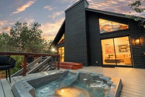 Et moderne hus med jacuzzi på terrassen, en trappe og et stort vindue med udsigt over indretningen.
