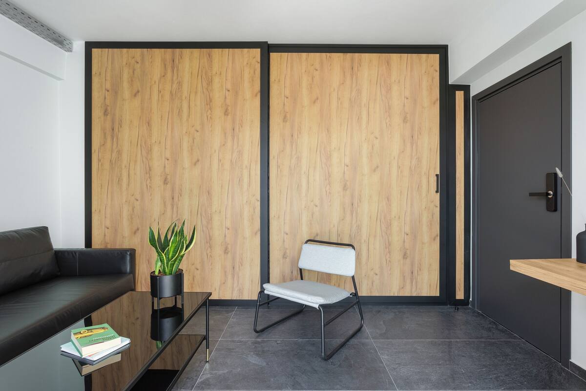 Ein modernes Zimmer mit einer schwarzen Ledersofa, einem Glastisch mit einem Buch, einem weißen Klappsessel und einer Holztrennwand.