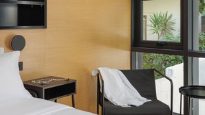 A modern hotel room with a bed, a chair, a small table, and a TV mounted on the wall. - THE URBANIST inner city residences (Ioannina)