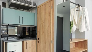 A compact kitchen with a built-in fridge, a microwave, and a small oven. There is a wooden wardrobe and a mirror with a coat rack. - THE URBANIST inner city residences (Ioannina)
