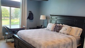 A bedroom with a large bed, a desk, a chair, a ceiling fan, and a window with a view of the outdoors. - Spacious 4-bedroom condo with space for your boat or to relax on Lake Conroe. (Montgomery)