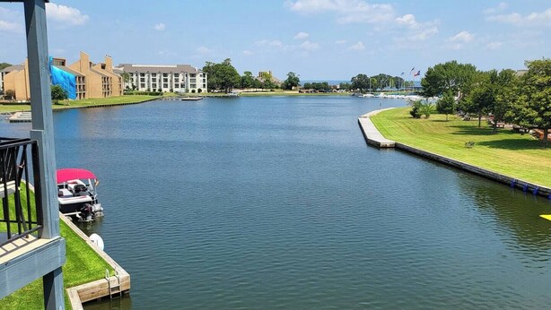 A river with a dock and a boat, surrounded by buildings and greenery. - Spacious 4-bedroom condo with space for your boat or to relax on Lake Conroe. (Montgomery)