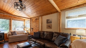 A cozy cabin interior with a wooden ceiling, a brown leather sofa, a beige sofa, and a fireplace. - Evergreen Escape -Fishing - Boating - Yellowstone - Hiking, Atving & Kayaking. (Island Park)