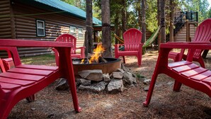 A log cabin with a fire pit surrounded by red Adirondack chairs. - Evergreen Escape -Fishing - Boating - Yellowstone - Hiking, Atving & Kayaking. (Island Park)