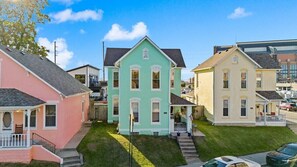 Une rangée de maisons à trois étages, avec une maison au toit vert au centre, chacune ayant un porche à l’avant et un petit jardin.