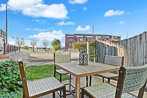 An outdoor patio with a wooden table and chairs, a lantern, and a view of a building in the background.