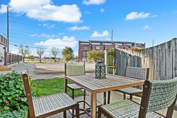 Une terrasse extérieure avec une table et des chaises en bois, une lanterne et une vue sur un bâtiment en arrière-plan.