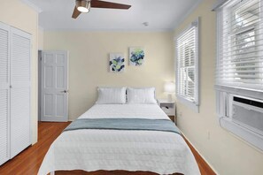 A bedroom with a bed, a ceiling fan, a window with blinds, and two wall art pieces. - Knowles Main House with Pool (Key West)