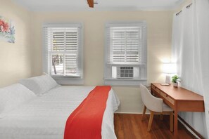 A bedroom with a bed, a desk, and two windows with blinds.