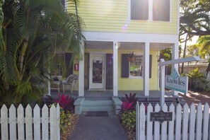 A yellow house with a porch, a sign reading 'Knowles House,' and a white picket fence.