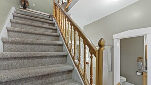 Un escalier recouvert de moquette, avec des balustrades en bois, mène à une salle de bain équipée de toilettes et d’un porte-serviettes.