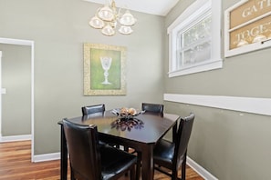 A dining area with a dark wooden table and chairs, a chandelier, and a framed picture on the wall.