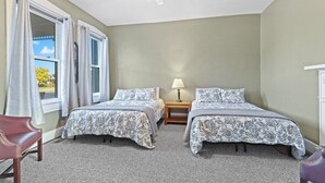 Une chambre avec deux lits, un ventilateur de plafond, une table de chevet avec une lampe et une fenêtre avec des rideaux.
