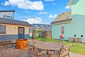 A backyard with a round metal table and chairs, a wooden barrel, and a blue building with a window.
