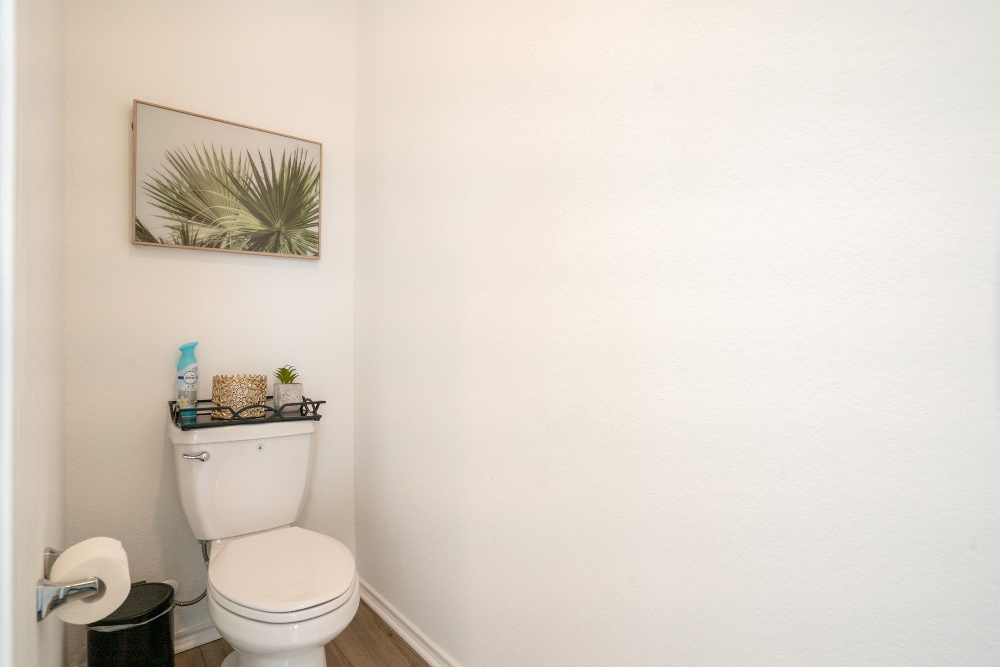 A small bathroom with a toilet, a trash can, and a shelf with toiletries.