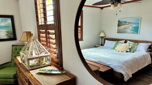A bedroom with a bed, a green chair, a wooden dresser, a mirror, and a ceiling fan. - Boomerang Bungalow - Cozy, quiet retreat on Saint Augustine's Anastasia Island!  (St. Augustine)