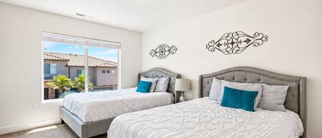 A bedroom with two beds, a window, and decorative wall art.