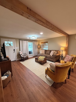 A living room with a wooden floor, a sofa, a yellow armchair, a coffee table, and a television.