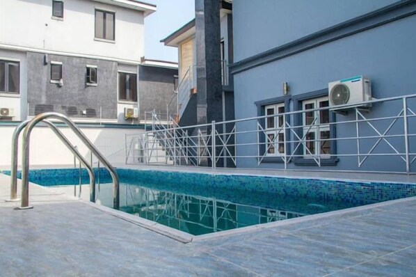 Une piscine avec un escalier en métal et une terrasse carrelée.
