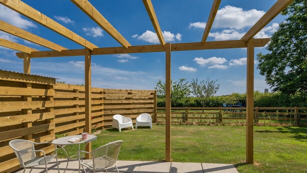 Ein überdachter Patio-Bereich mit einer Holzw pergola, einem kleinen runden Tisch und zwei Stühlen.