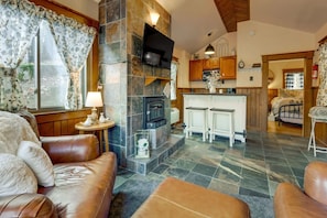 A cozy living room with a fireplace, leather sofas, and a dining area with bar stools. - Village 37 Stone Cabin with Private Hot Tub (Bryson City)