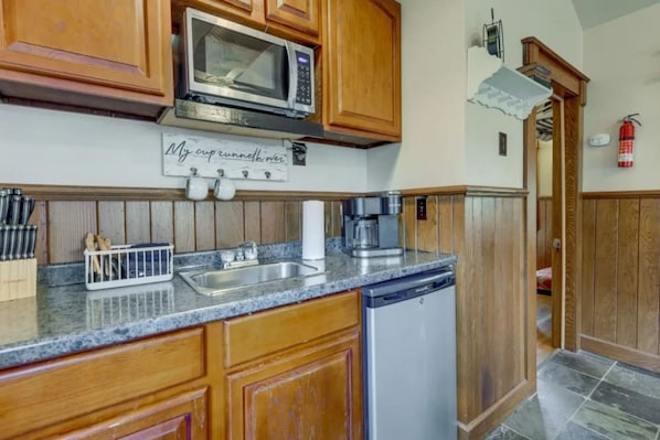 A kitchen with wooden cabinets, a microwave, a coffee maker, and a dishwasher. - Village 37 Stone Cabin with Private Hot Tub (Bryson City)