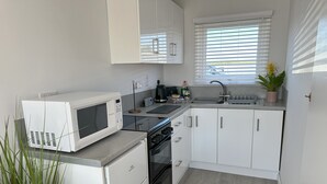 A compact kitchen with white cabinets, a microwave, a stove, and a sink. - Mardle | Modern Dog Friendly Chalet, Walk to Hemsby Beach, Shops & Cafés (Hemsby)