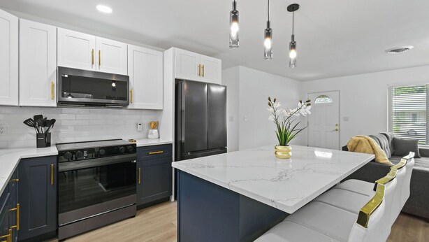 A modern kitchen with white cabinets, a black refrigerator, stainless steel appliances, and a marble island. - Incredible 4-bedroom home in Tequesta FL with AC, WiFi and absolute comfort. (Tequesta)