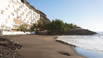 Un hôtel situé sur la côte, avec une façade blanche, une plage de sable et une falaise rocheuse.