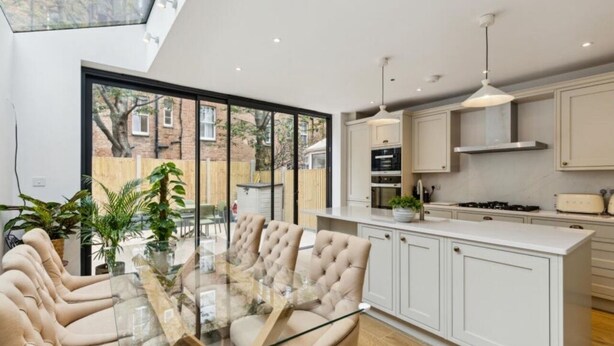 Una cocina moderna con muebles blancos, una isla central y un comedor con mesa de vidrio y sillas acolchadas.