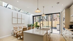 Cocina moderna con una isla central, un comedor con mesa de vidrio y vistas al exterior.