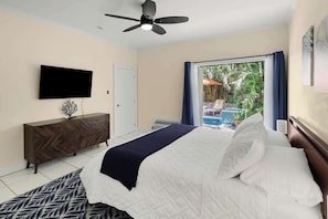 A hotel room with a bed, a ceiling fan, a TV, a wooden dresser, and a view of a pool.