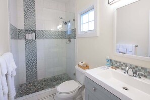 A bathroom with a shower, toilet, sink, and a window.