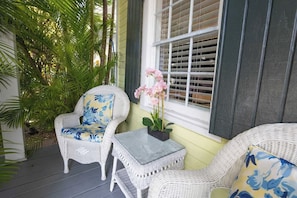 A porch with wicker furniture, a small table, and a window with shutters.