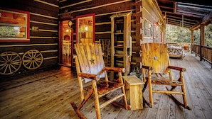 A rustic cabin with wooden rocking chairs and a wooden table on the porch.