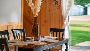 Une table à manger en bois, quatre chaises, un vase contenant des plumes d’herbe des pampas et une horloge au mur.