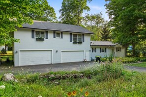 Ein zweigeschossiges Haus mit Garage, einer kleinen Veranda und einem Garten mit Wildblumen.